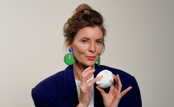 Denise Boomkens, author and age-positive advocate, holding a white jar of skincare cream and smiling.